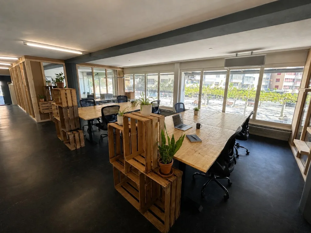 Espace de coworking à Sion avec postes de travail partagés et grandes fenêtres sur la Place du Midi
