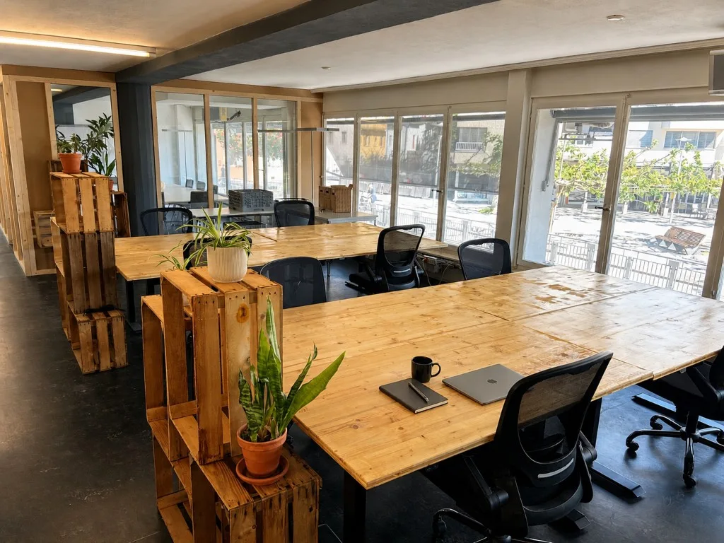 Postes fixes dans un bureau partagé à Sion avec tables en bois, plantes et lumière naturelle